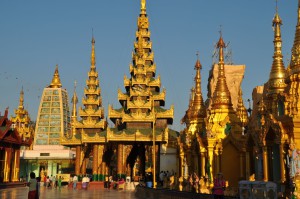 Reise in Myanmar in Asien. Die goldenen Dächer und die zahlreichen Besucher der weitläufigen Tempelanlage bei der Shwedagon Pagode in der burmesischen Stadt Yangon werden von der Abendsonne beschienen.
