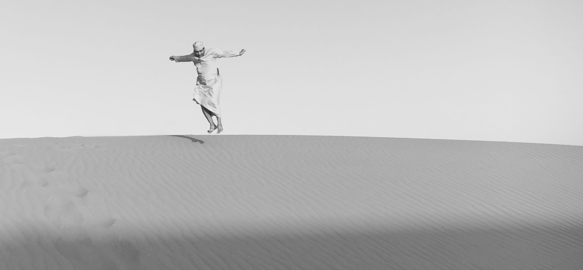 Reise in Oman im Orient. Deutschsprachiger Reiseleiter in traditioneller Kleidung springt über eine Sanddüne in der Wüste Wahiba Sands.