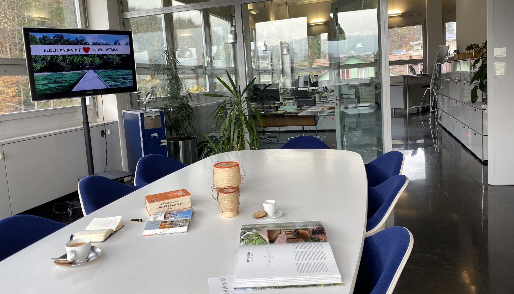 Geräumiges Büro von Simtis Reisen weltweit, in Sitzungszimmer liegen Reiseführer, Karten, und ein Kaffee bereit, am Fernsehbildschirm steht der Schriftzug "Reiseplanung mit Liebe zu den Details".