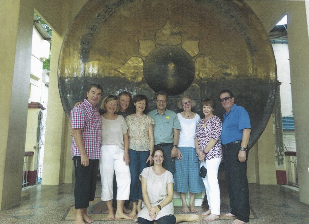 Postkarte von einer Myanmar Gruppenreise von zufriedenen Simtis Kunden. Abgebildet ist ein Gruppenbild von allen neun Teilnehmern inklusive Meret Deeg, die in der Mitte auf dem Boden sitzt.