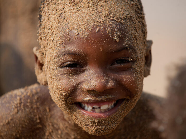 Reise in Sao Tome und Principe in Afrika. Ein einheimisches Kind ist im ganzen Gesicht mit Sand bedeckt und strahlt in die Kamera.
