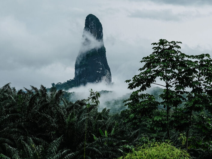 Reise in Sao Tome und Principe in Afrika. Die Basaltnadel Pico Cao Grande ragt aus dem Urwald empor und wird von Dunst umgeben.