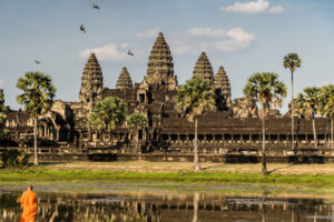 Tempelanlage Angkor Wat vor einem See mit Mönch und Palmen